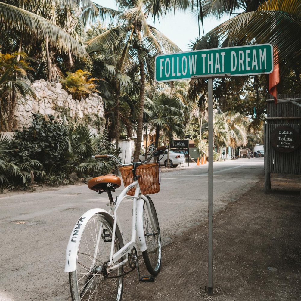 A bicycle on dirt street by sign that says follow your dreams